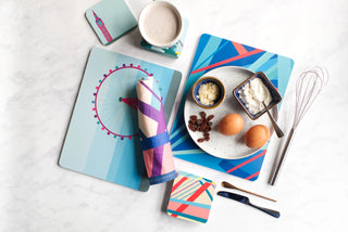 Colourful blue placemats, coasters and a rolled tea towel alongside a plate of ingredients for pancakes