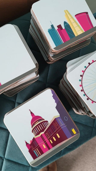 Four stacks of coasters sit on a velvet bench, each illustrated with a different London landmark.