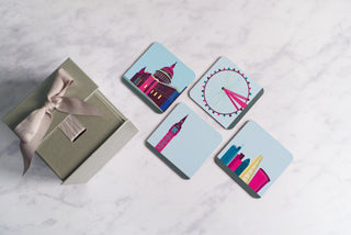Four London landmark coasters on a marble table beside a silver gift box with ribbon.