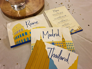 A selection of wedding table name signs and menu from a travel themed wedding. The illustrated signs show Rome, Madrid and Thailand.