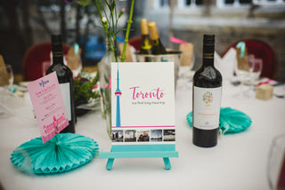 Illustrated table name 'Toronto' sits on a white table cloth beside bottles of wine and a wedding day menu.