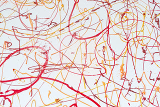 Detail of ribbons of red, yellow and orange paint scattered across a white canvas.