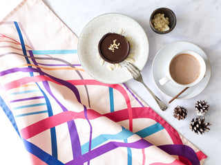 Colourful blue placemats, coasters and a rolled tea towel alongside a plate of ingredients for pancakes
