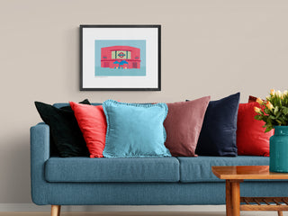 Framed art print of Balham Underground Station above a blue sofa. The illustration complements the colours of the sofa and cushions.