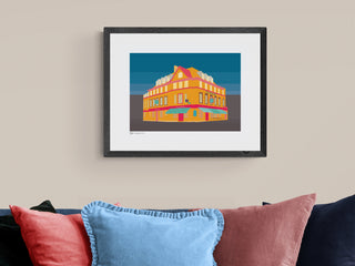 Illustrated art print of the Bedford Pub in Balham above a sofa with cushions.