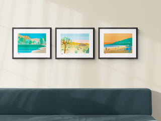 Triptych of three bespoke art prints, each illustrating a destination in California. They are hanging above a dark green sofa.