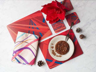 Red placemats and coasters with a geometric pattern sit on a table with a folded tea towel. 