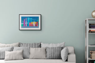 Framed New York City print with a skyline of landmarks above a sofa. Illustrated by South Island Art, the print hangs on a light green wall that complements the blue, purple and green colours in the print.