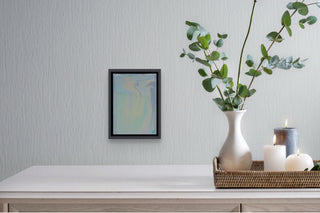 Gentle fluid painting in a grey floater frame above a dining table with vase and lit candles.