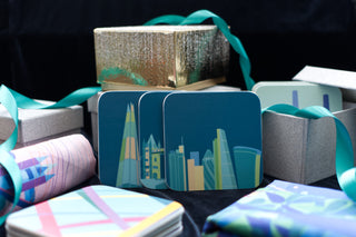 Teal coasters illstrated with London Landmarks propped up against sparkly silver and gold gift boxes. 