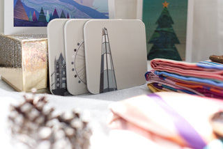 Black and white coasters illustrated with London Landmarks propped up against a sparkly gold gift box .