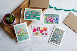 Set of 5 greetings cards with a botanical theme on a marble table with a wooden tray, plant pot, pen and envelopes.