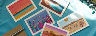 Illustrated greetings cards depicting different types of landscapes are scattered over a blue background.