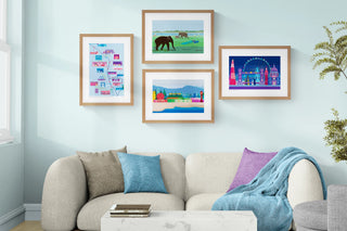 Colourful framed artworks on a light blue wall above a beige sofa with cushions.