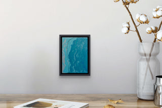 turquoise and grey fluid painting by south island art hanging on pale grey wall above a wooden table.