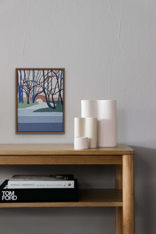 Framed Woodlands painting by South Island Art above a wooden table with vases on it.